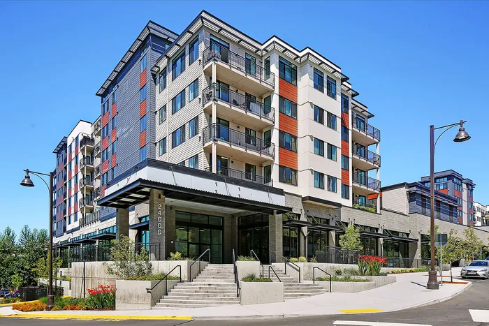 Modern multi-story apartment building with vibrant facade, featuring spacious balconies and landscaped surroundings under a clear blue sky.