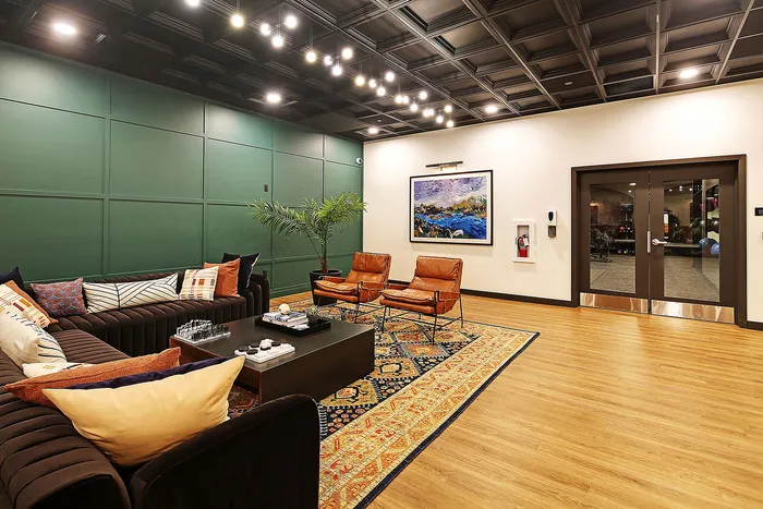 Elegant and inviting lounge area featuring plush sofas with colorful cushions, stylish leather chairs, vibrant artwork, and a sleek coffee table on an ornate rug.