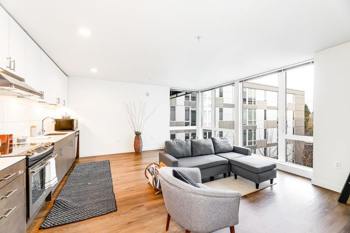 Modern open-concept apartment living room with floor-to-ceiling windows, sleek kitchen, and stylish gray furniture.
