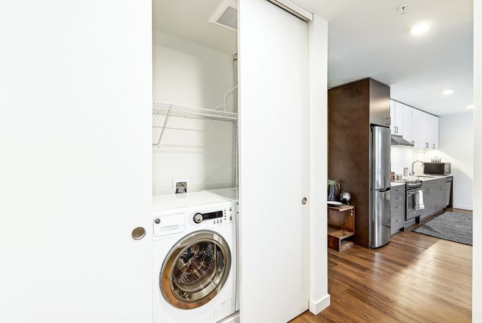 Modern apartment with sleek kitchen featuring stainless steel appliances and convenient in-unit washing machine, highlighted by warm wood flooring.
