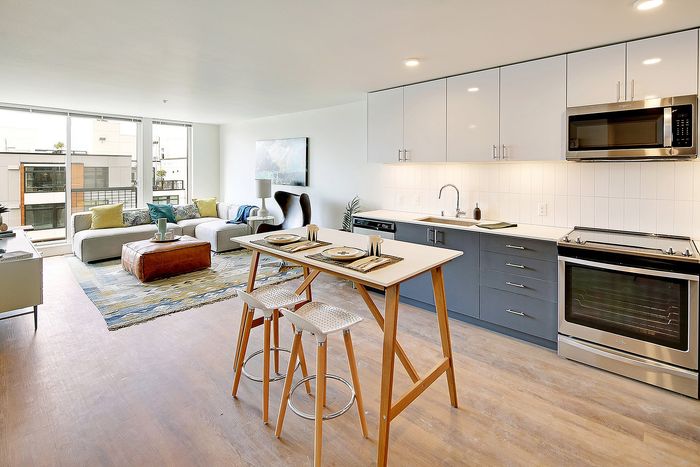 Modern open-concept apartment with a sleek kitchen, stylish breakfast bar, and bright living area featuring floor-to-ceiling windows.