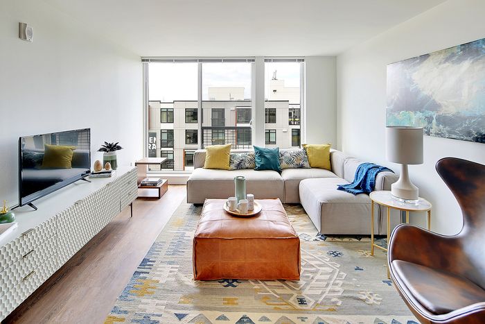 Bright and modern living room with large windows, stylish sectional sofa, and chic decor, overlooking a cityscape.