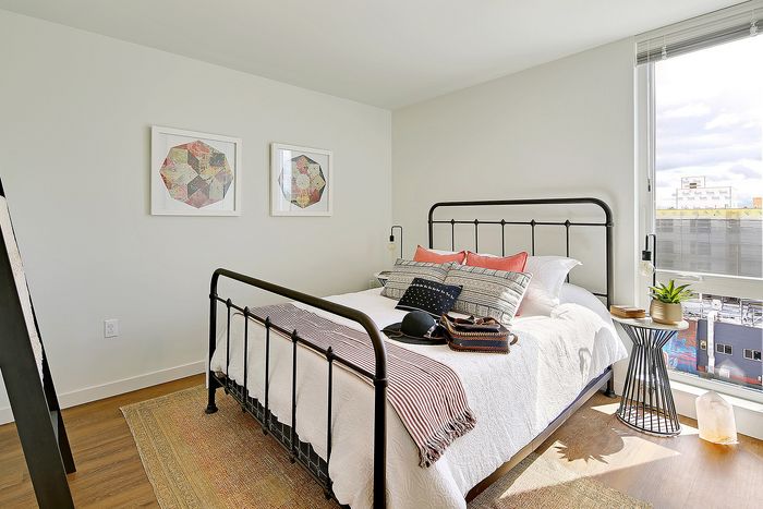 Bright and inviting bedroom with stylish iron bedframe, vibrant pillows, and large window offering city views.