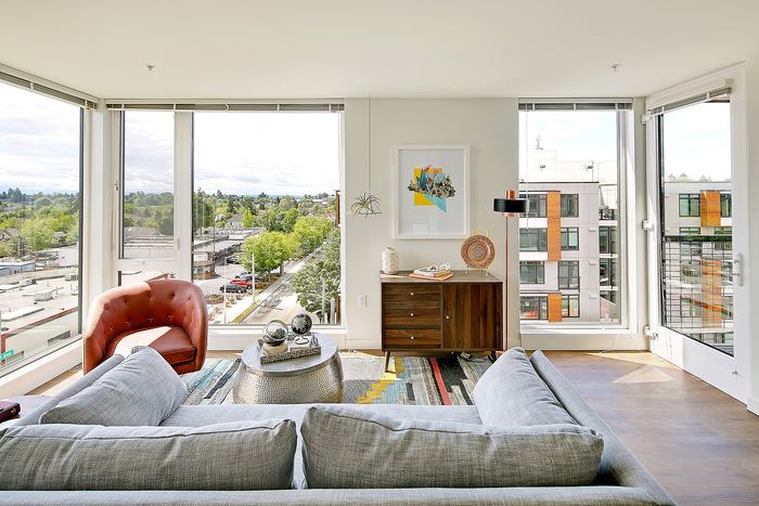 Bright and modern living room with panoramic city views, featuring a cozy gray sofa, stylish red armchair, and chic decor.
