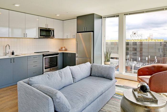 Bright and modern open-concept kitchen with a stylish grey and white color scheme, comfortable seating, stainless steel appliances, and large windows offering city views.