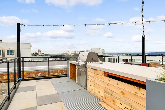 Chic rooftop patio with modern grill and stunning urban skyline views, featuring string lights and cozy seating.