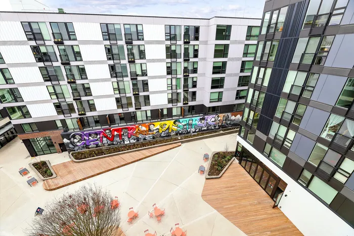 Vibrant urban apartment complex with colorful mural and modern architecture, featuring an inviting courtyard with seating.