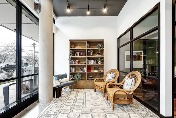 Welcoming reading nook with natural light, featuring rattan chairs, a plush armchair, and a stocked wooden bookshelf.