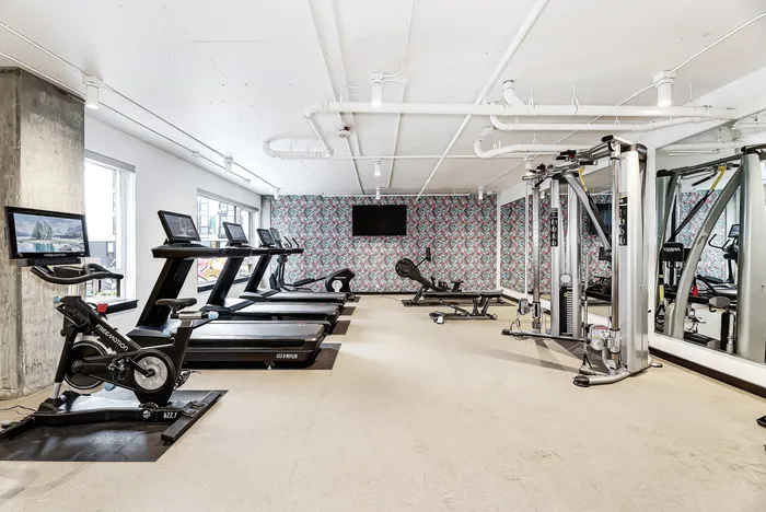 Modern fitness center with state-of-the-art exercise equipment, including treadmills, stationary bikes, and a multi-use weight machine, set against a stylish patterned wall.