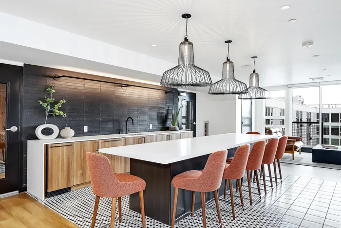 Modern kitchen featuring sleek wooden cabinetry, a spacious white island with orange chairs, and stylish pendant lighting in a bright open-concept layout.
