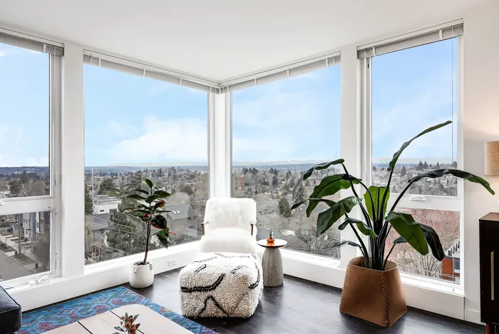 Bright and airy living space with panoramic city views, featuring large windows, cozy seating, and lush green plants.