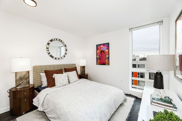 Bright modern bedroom with stylish decor, featuring large windows, elegant lamps, and eye-catching artwork.