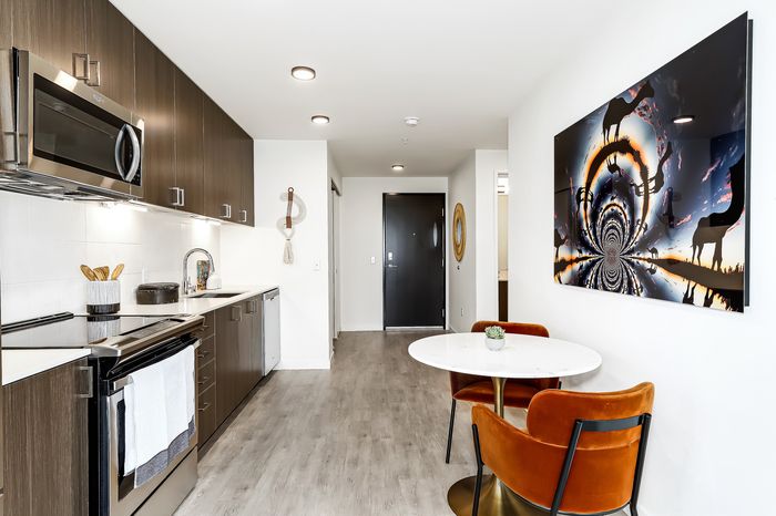Modern kitchen featuring sleek dark cabinets, stainless steel appliances, and a chic dining area with vibrant orange chairs and a unique wall art piece.