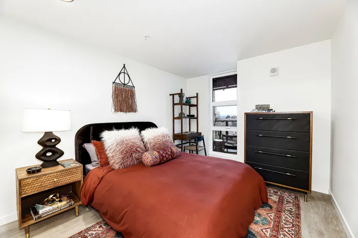 Chic bedroom featuring a luxurious bed with textured pillows, stylish decor, and plenty of natural light through a large window.