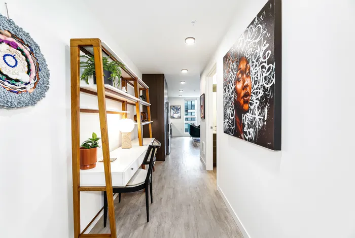 Sleek and stylish apartment hallway with modern artwork and a cozy workspace featuring elegant wooden shelves and vibrant plants.