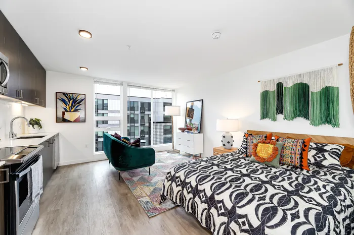 Modern studio apartment with open-concept layout featuring a cozy bedroom area with vibrant decor, compact kitchen with sleek cabinetry, and a stylish living space with large windows offering natural light and city views.