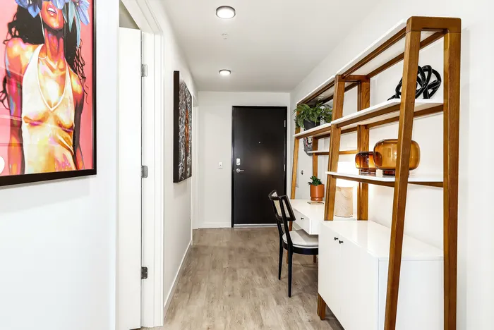 Chic apartment hallway featuring artistic wall decor, modern shelving with plants and decor, and a cozy work nook.