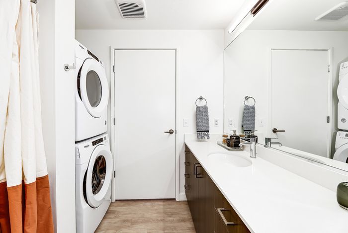 Bright and modern bathroom featuring a sleek vanity with ample storage, and a convenient stacked washer and dryer for efficient living.