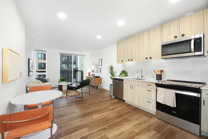 Modern open-concept kitchen and living area with sleek appliances, warm wood flooring, and abundant natural light from large windows.