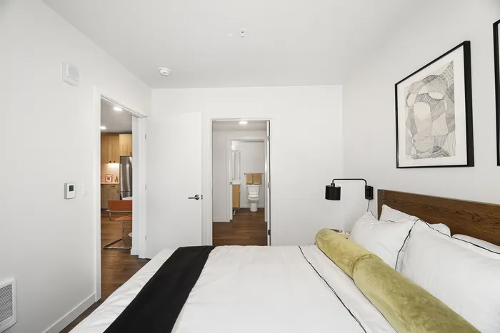 Elegant bedroom with stylish decor, featuring a comfortable bed, modern art, and a view into a sleek bathroom and kitchen area.