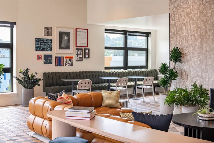 Chic apartment interior showcasing a cozy lounge with a plush leather sofa, stylish wall art, and vibrant potted plants, enhanced by natural light through large windows.