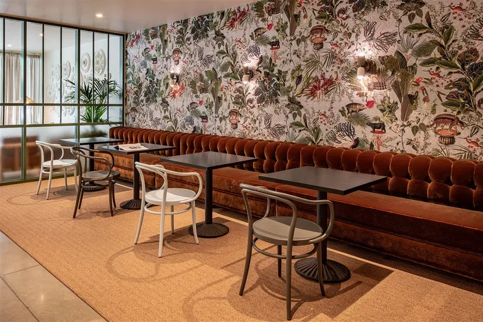 Chic dining area with plush velvet bench seating, stylish modern tables, and vibrant tropical wallpaper offering an inviting and sophisticated atmosphere.