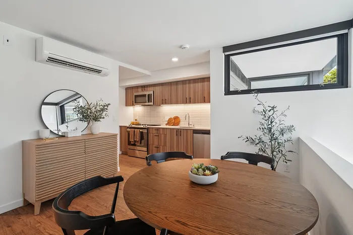 Contemporary kitchen and dining area with sleek wooden cabinets, stainless steel appliances, and a round wooden table with stylish black chairs.