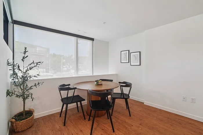Bright dining area with modern black chairs, a round wooden table, and abundant natural light from large windows.
