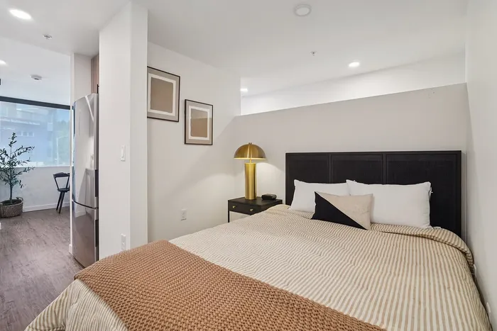 Inviting bedroom with soft lighting, modern d&eacute;cor, and a comfy bed, connected to an open living area with stylish furnishings.