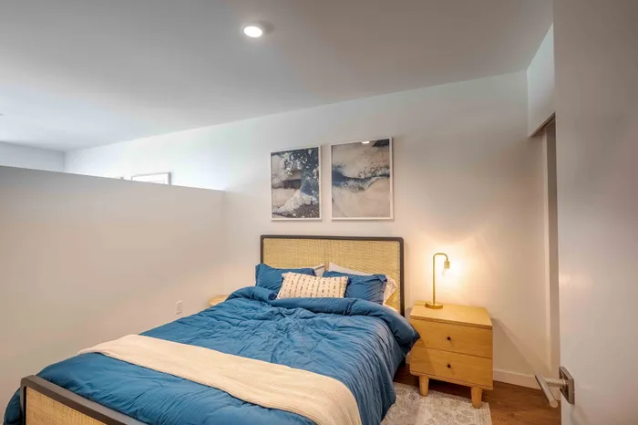 Cozy bedroom with stylish decor including blue bedding, wooden nightstand with lamp, and modern abstract wall art.