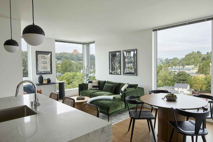 Modern apartment with a sleek kitchen, stylish green velvet sectional, and large windows offering stunning views.