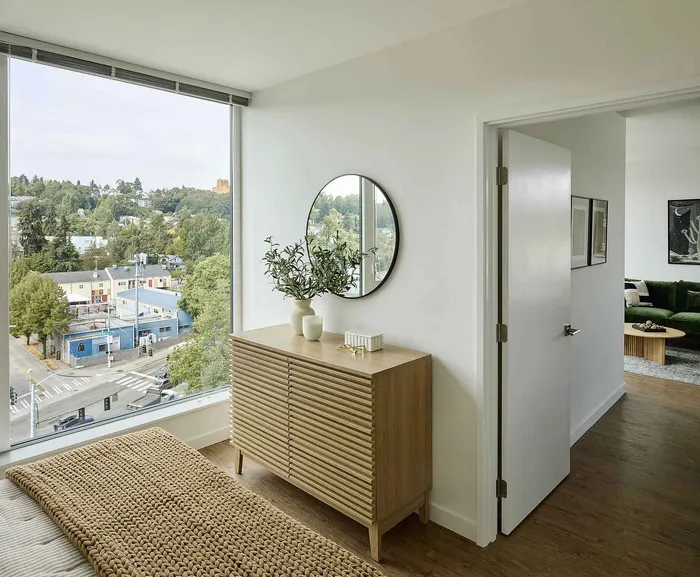 Chic apartment interior featuring a cozy hallway with a wooden cabinet, large window offering scenic views, and a glimpse into a stylish living area.