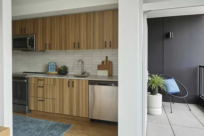 Modern kitchen with sleek wooden cabinets, stainless steel appliances, and a cozy balcony featuring stylish outdoor seating and a potted plant.