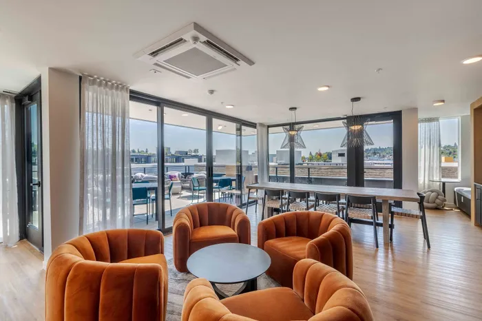 Spacious and stylish living area featuring plush orange chairs, large windows with scenic views, and a modern dining space with chic pendant lighting.