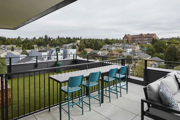 Chic rooftop patio with modern seating, offering picturesque views of a vibrant neighborhood and lush greenery.