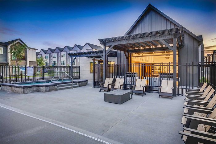 Charming outdoor area with modern patio seating and hot tub against a backdrop of stylish residential buildings at sunset.