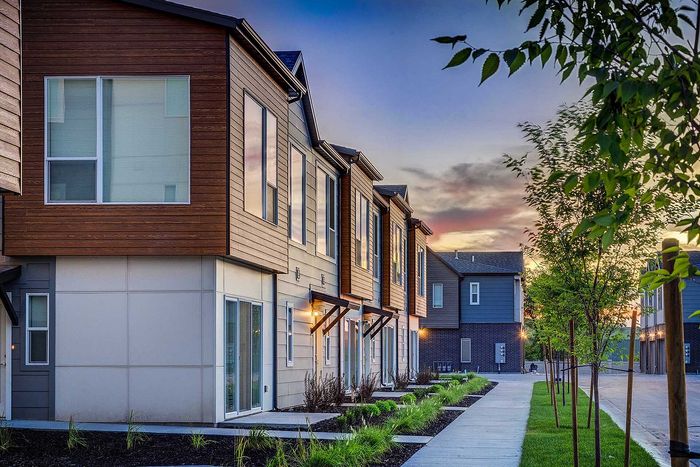 Modern townhomes with sleek wooden siding and large windows, set against a beautiful sunset backdrop, offering a stylish and serene living environment.