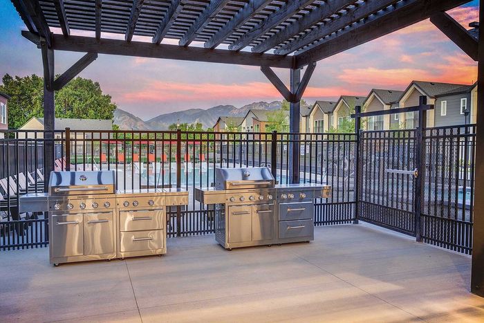 Charming outdoor grilling station with stainless steel barbecues under a pergola, overlooking a serene pool and mountain views.