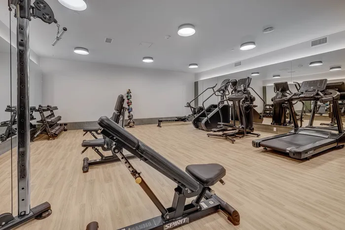 Modern fitness center with state-of-the-art equipment, including treadmills and a weight station, on stylish wood flooring.