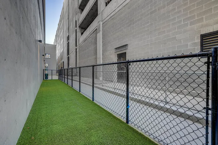 Modern urban outdoor space featuring a secure fenced area with artificial grass for versatile use.