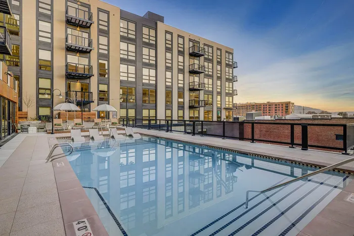 Modern urban apartment building with a luxurious pool, featuring inviting poolside loungers and stylish balconies at sunset.