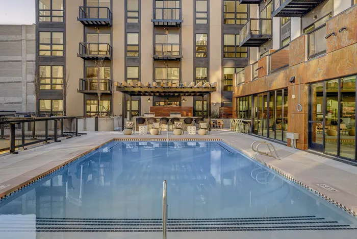 Luxurious apartment complex featuring a sparkling outdoor pool, modern architecture, and stylish seating area.