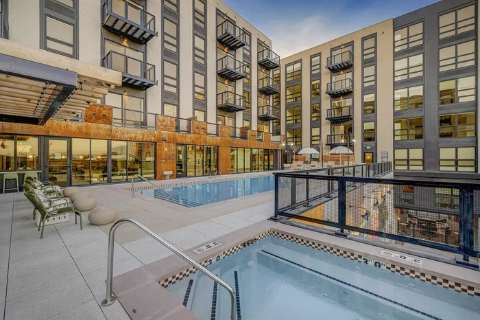 Modern apartment complex with a luxurious outdoor pool and hot tub, surrounded by elegant seating and stylish balconies.