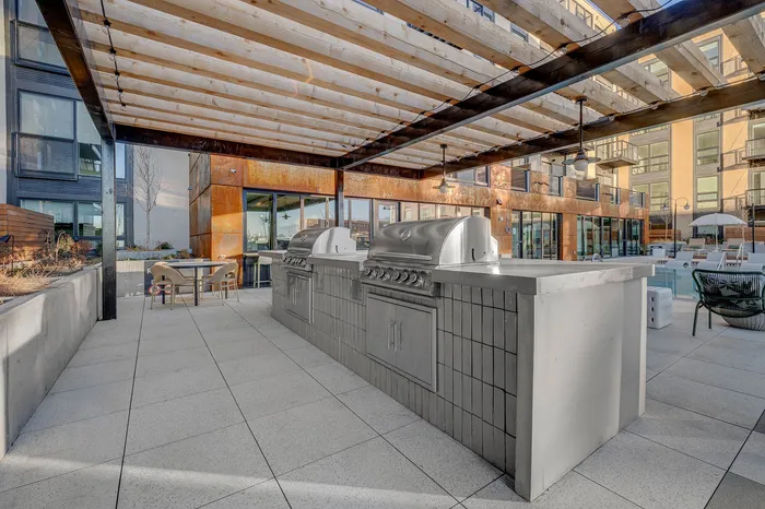 Modern outdoor kitchen area with sleek stainless steel grills under a stylish pergola, perfect for entertaining.