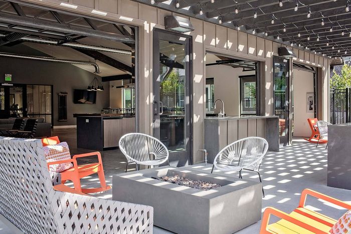 Contemporary outdoor lounge with cozy seating, modern fire pit, and stylish lighting, opening to a chic indoor kitchen space.