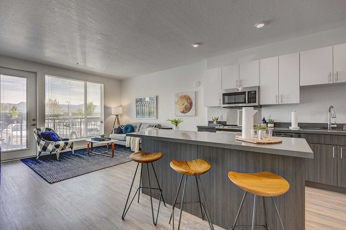 Modern open-concept kitchen and living area featuring sleek cabinetry, stylish bar stools, and floor-to-ceiling windows offering abundant natural light.