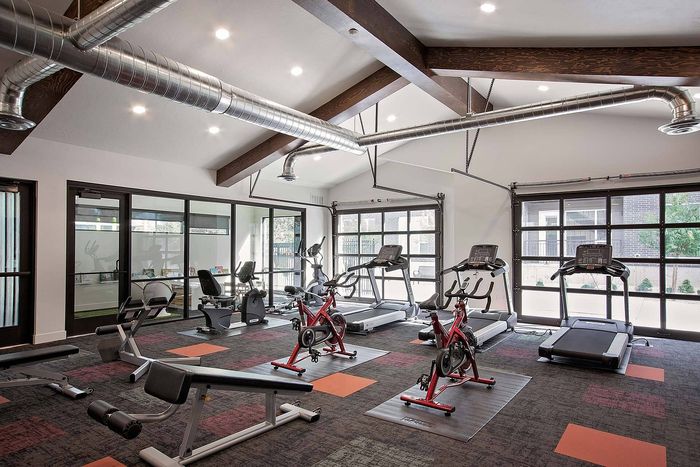Modern fitness center with high ceilings, featuring red exercise bikes, treadmills, and weight benches in a bright and airy space.