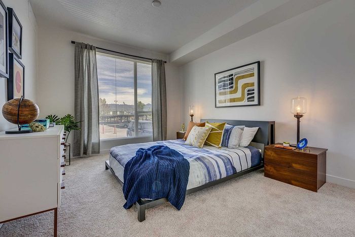 Inviting bedroom with a modern bed, vibrant pillows, and a large window illuminating the cozy atmosphere.