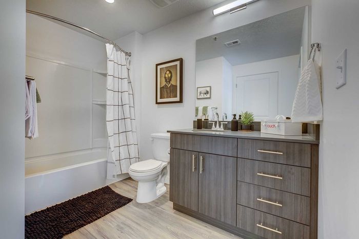 Modern bathroom with sleek wooden vanity, stylish artwork, and plush decor, offering a serene spa-like atmosphere.