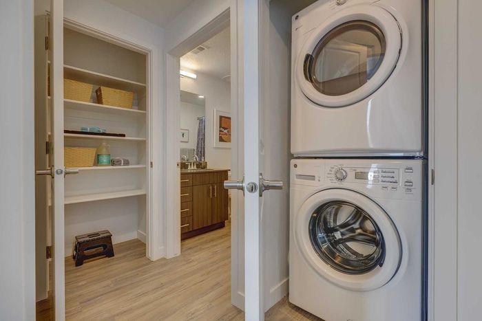 Modern apartment showcasing a convenient in-unit washer and dryer beside a spacious shelving unit and elegant bathroom view.